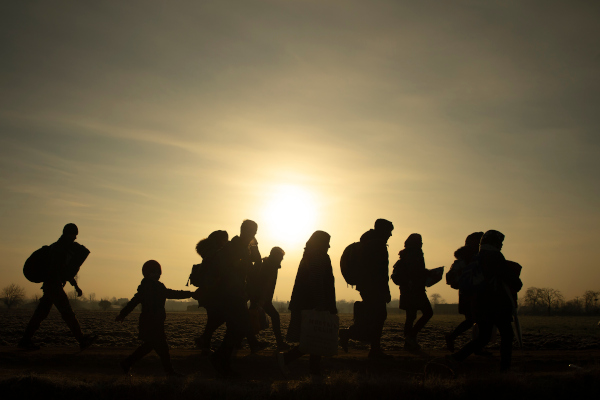Grupo de pessoas caminhando e luz do Sol ao fundo ilustrando o conceito de migração.
