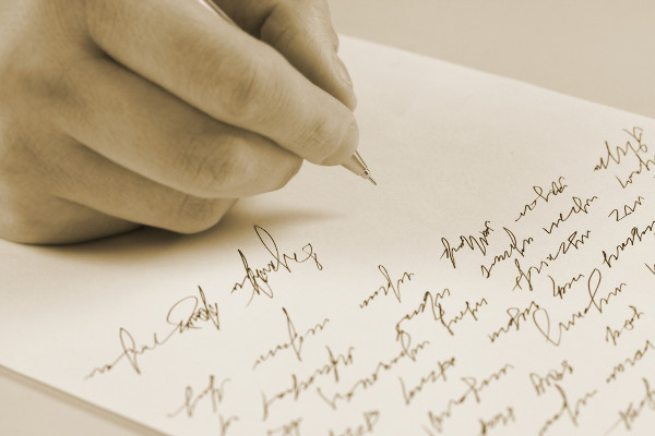 Mão escrevendo em uma folha de papel, em alusão a uma carta pessoal.