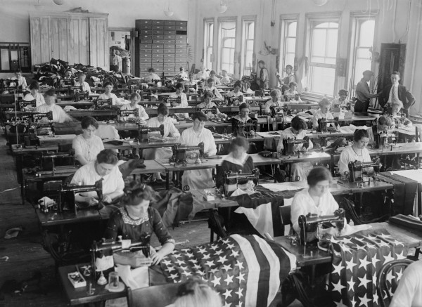 Mulheres costurando bandeiras dos Estados Unidos no modo de produção taylorista.
