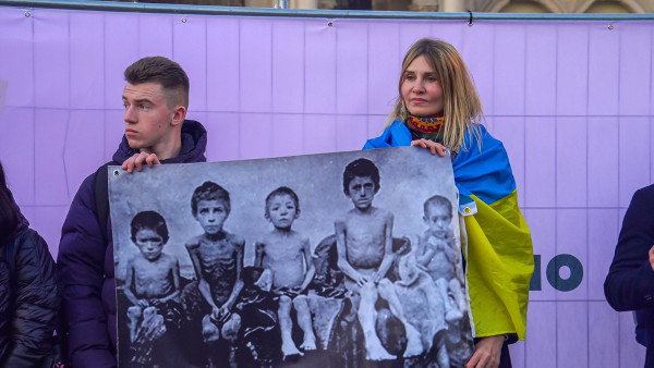 Pessoas segurando cartaz com fotos de vítimas do Holodomor.