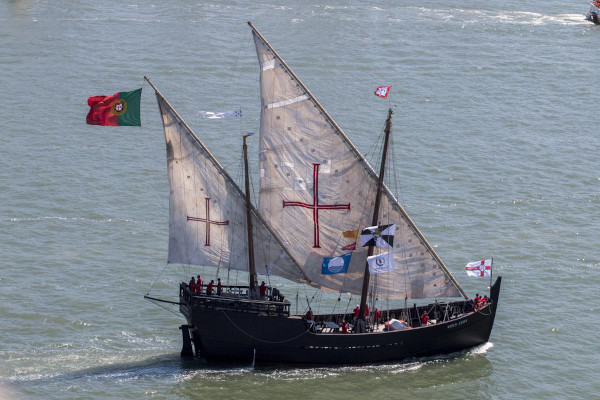 Caravela, com bandeira de Portugal, no mar, em referência à expansão marítima portuguesa.
