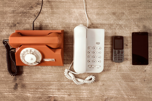 Diferentes aparelhos sobre uma mesa de madeira mostrando a evolução do telefone.