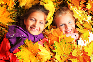 Meninas brincando em parque com folhas que mudaram de cor e caíram no outono